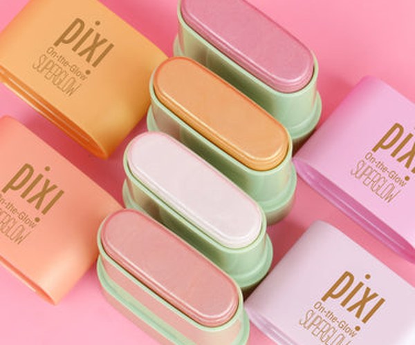 Pixi On-the-Glow Superglow highlight sticks in pastel shades arranged diagonally on a solid pink background. ad image